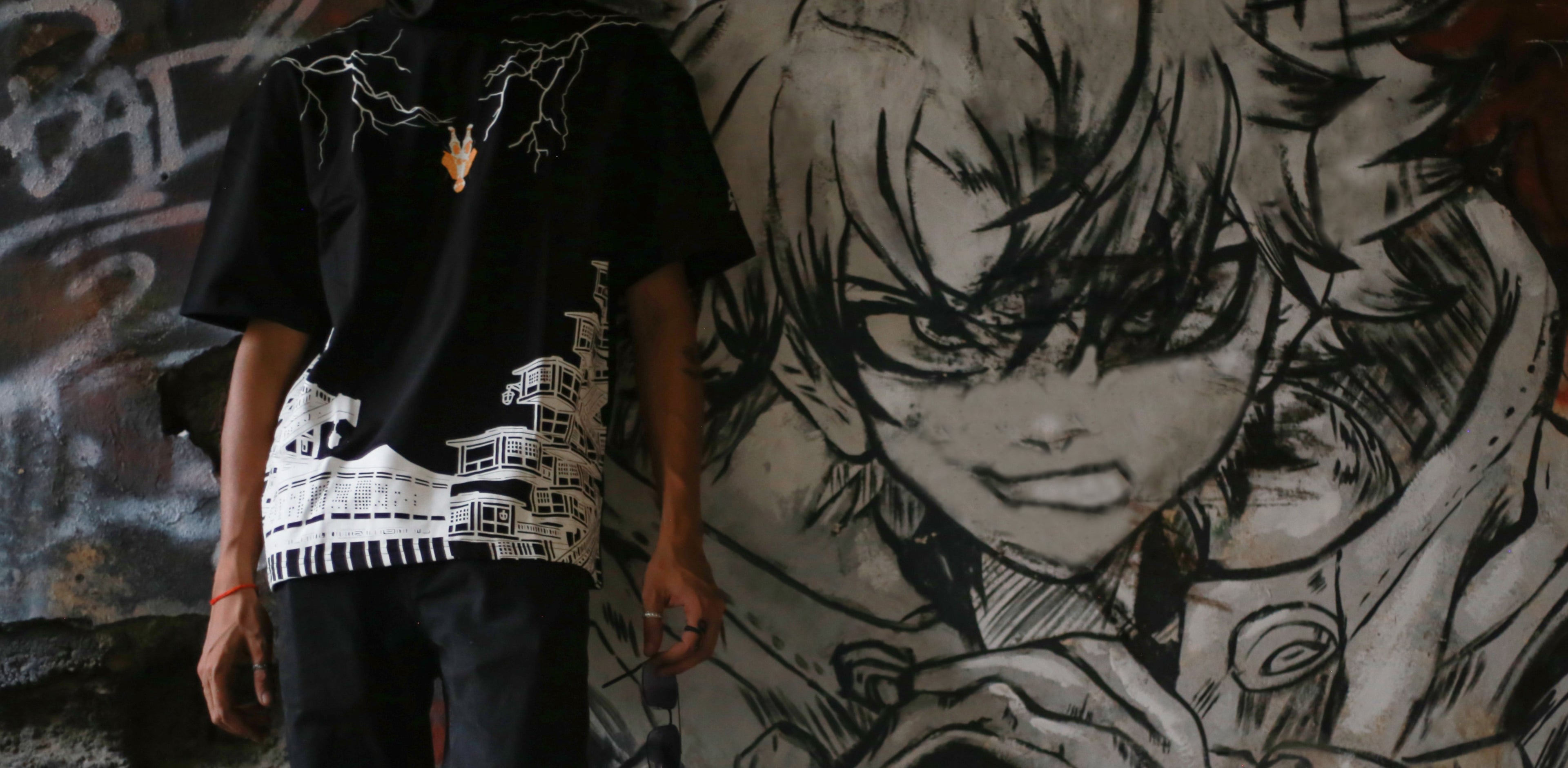 Alt text: Model wearing a black zenitsu demon slayer graphic anime streetwear t-shirt in front of a graffiti wall with anime art.