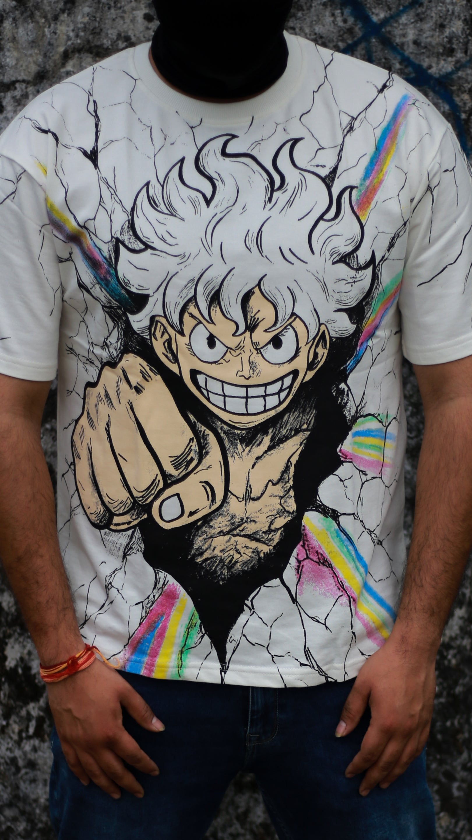Model wearing an oversized white anime graphic t-shirt inspired by Luffy from One Piece, featuring a bold Gear 5 style character print and urban streetwear aesthetic against a graffiti wall backdrop.